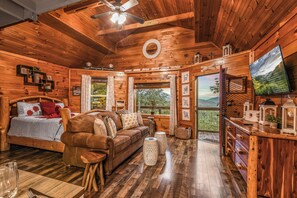 A wooden cabin interior with a bed, sofa, dining table, and a TV. - Lookout Point - Firepit, Pickle Ball, Balcony, Pet (Sevierville)