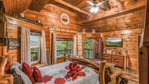 A wooden cabin bedroom with a bed, a dresser, a television, and a view of the outdoors. - Lookout Point - Firepit, Pickle Ball, Balcony, Pet (Sevierville)