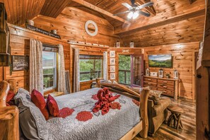 A wooden cabin bedroom with a bed, a dresser, a television, and a view of the outdoors. - Lookout Point - Firepit, Pickle Ball, Balcony, Pet (Sevierville)