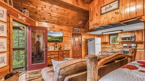 Interior de una cabaña con detalles de madera, una cocina con electrodomésticos modernos, un ventanal grande y una zona de estar acogedora.