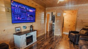 Un salon chaleureux avec une cheminée, un téléviseur fixé au mur et un plancher en bois.