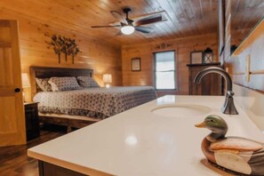 Interno di una baita in legno con un letto, un bagno con un lavandino e una decorazione a forma di anatra, e una ventola a soffitto.