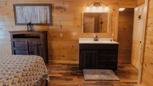 L’intérieur d’une cabane en bois, avec un lit, une commode, une coiffeuse avec un miroir et un petit tapis.
