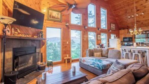 Un intérieur de chalet chaleureux avec une cheminée, un grand canapé, un coin repas et une cuisine.