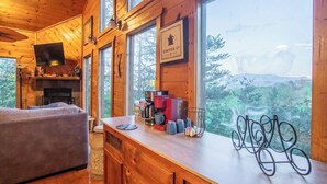 L’intérieur chaleureux d’un chalet avec des murs en bois, une grande fenêtre donnant sur la forêt, une cheminée et un coin café.