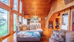 Une cabane en rondins spacieuse, dotée d’un salon confortable comprenant un canapé, une table à manger et un coin cuisine.