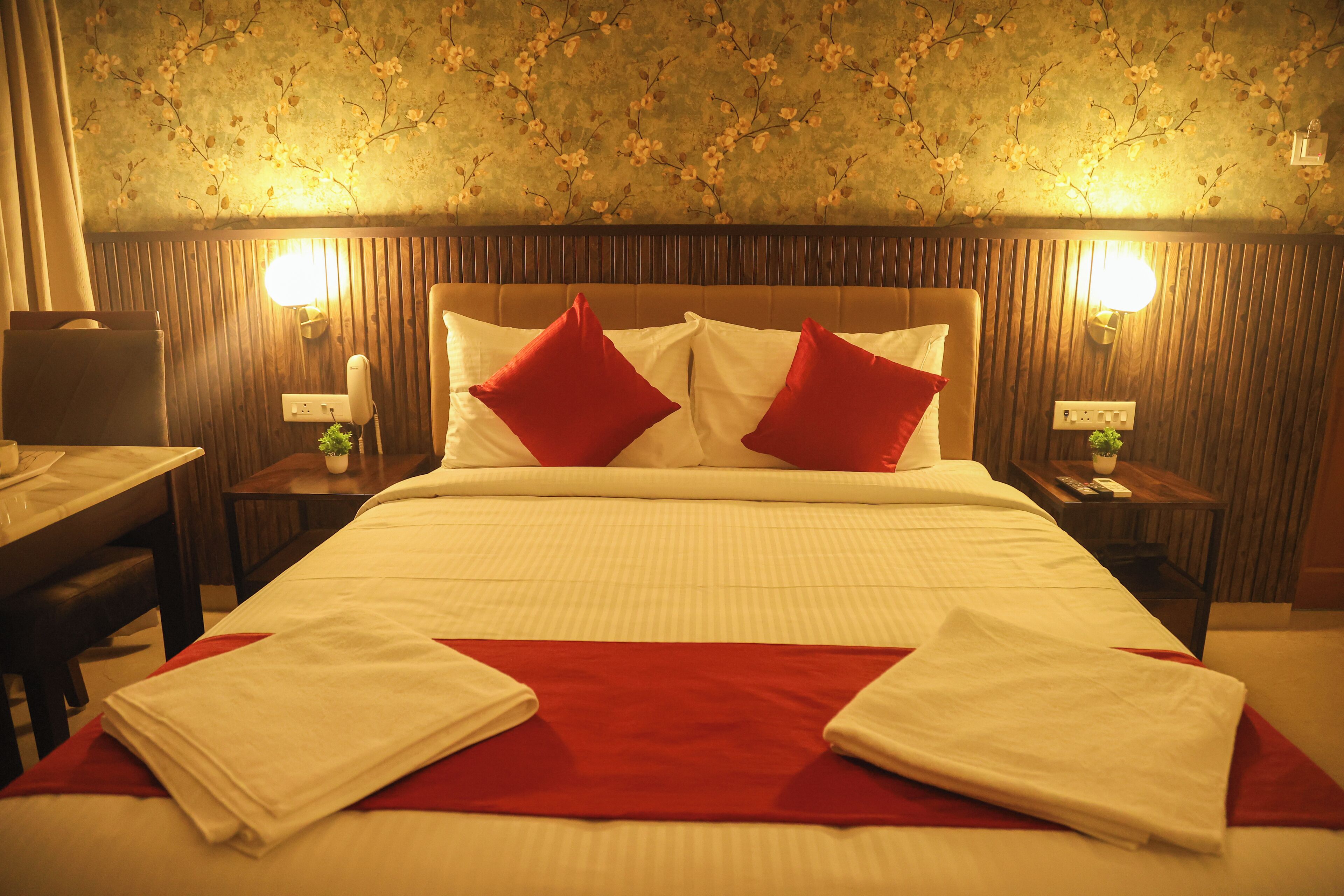 A hotel room with a bed, two bedside tables, a nightstand, a lamp, and a wall with floral wallpaper.