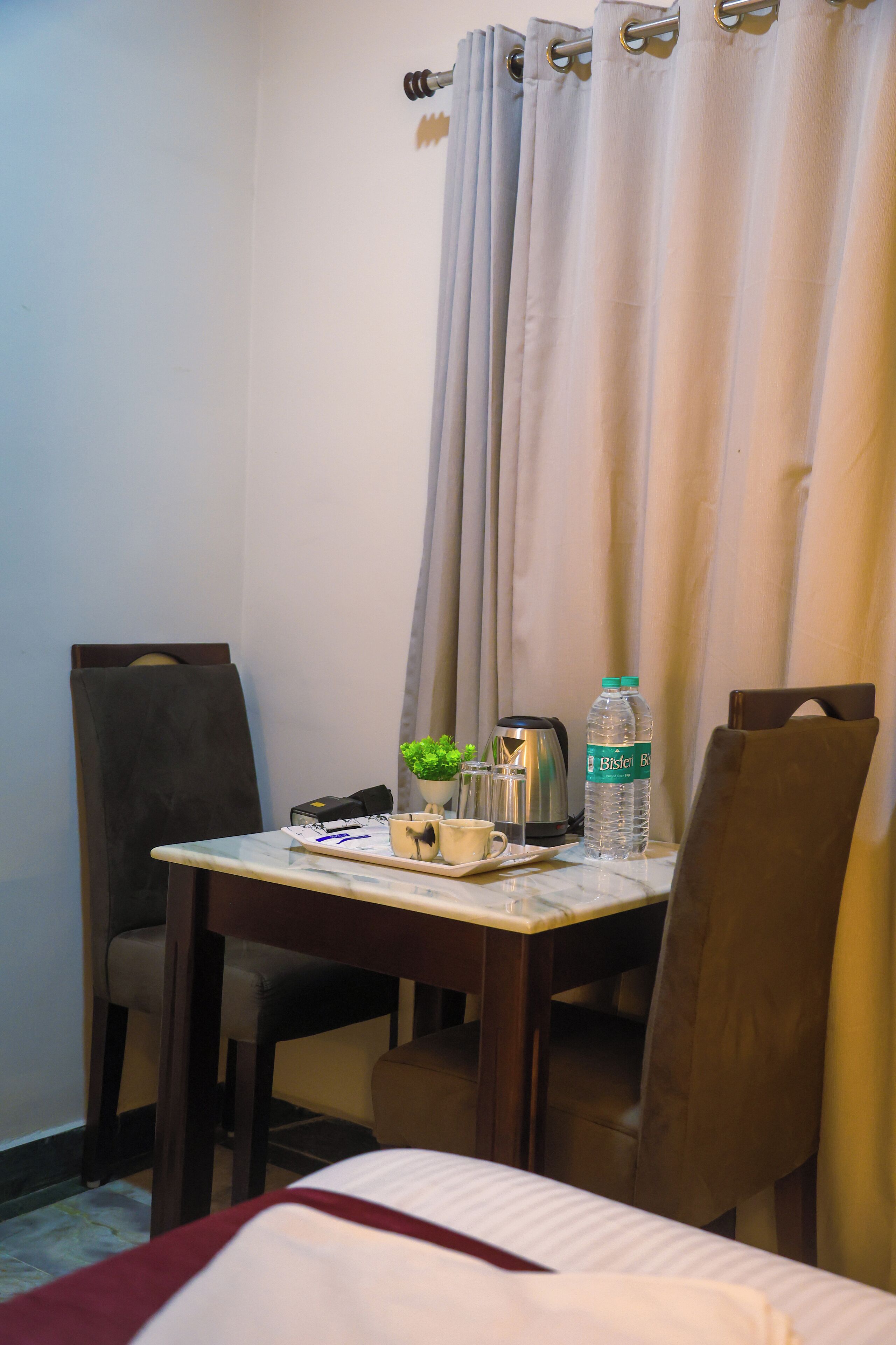 Une chambre d’hôtel avec un lit, une table sur laquelle se trouve une bouilloire, une bouteille d’eau et une petite plante.