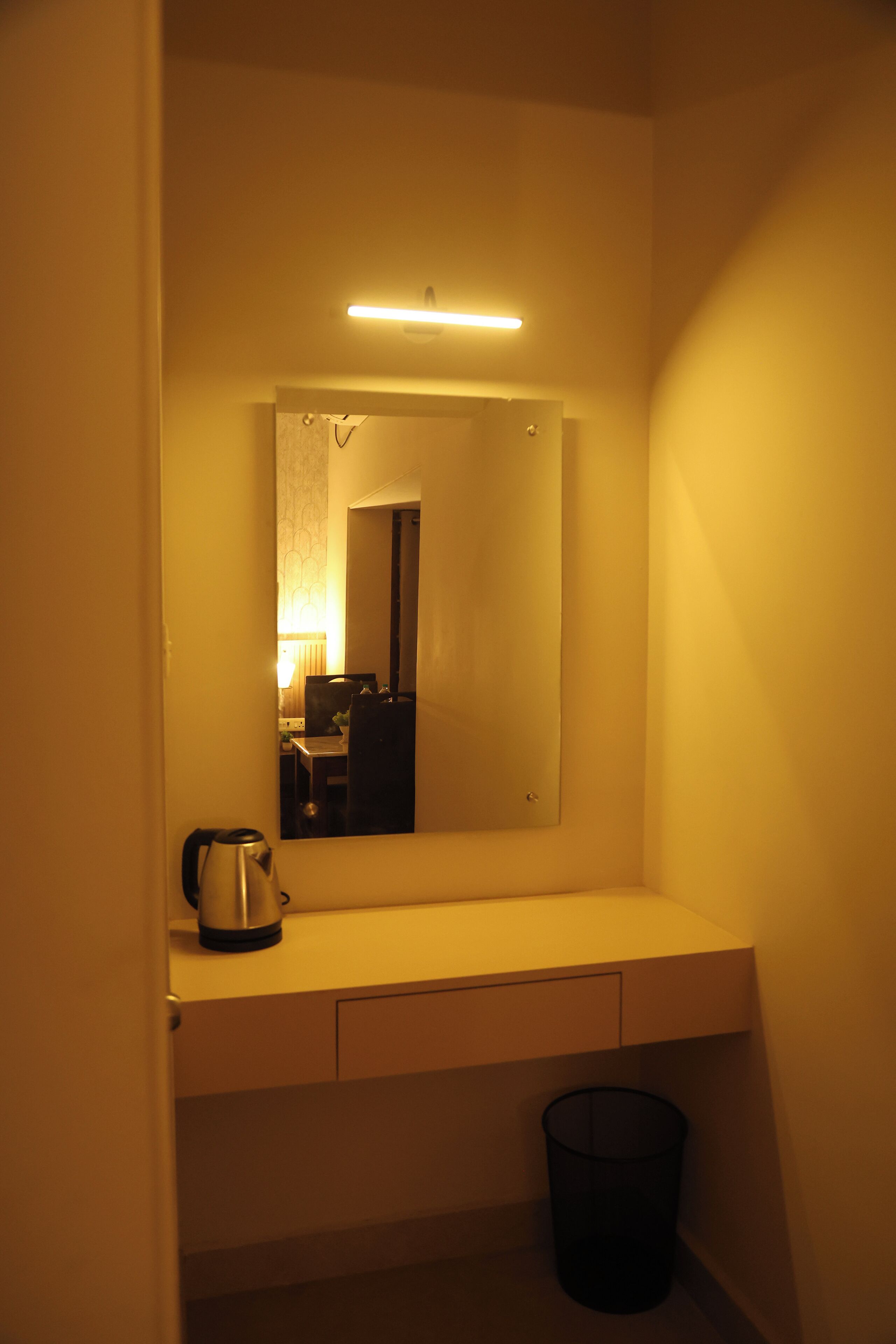 A small bathroom with a mirror, a sink, a kettle, and a trash bin.