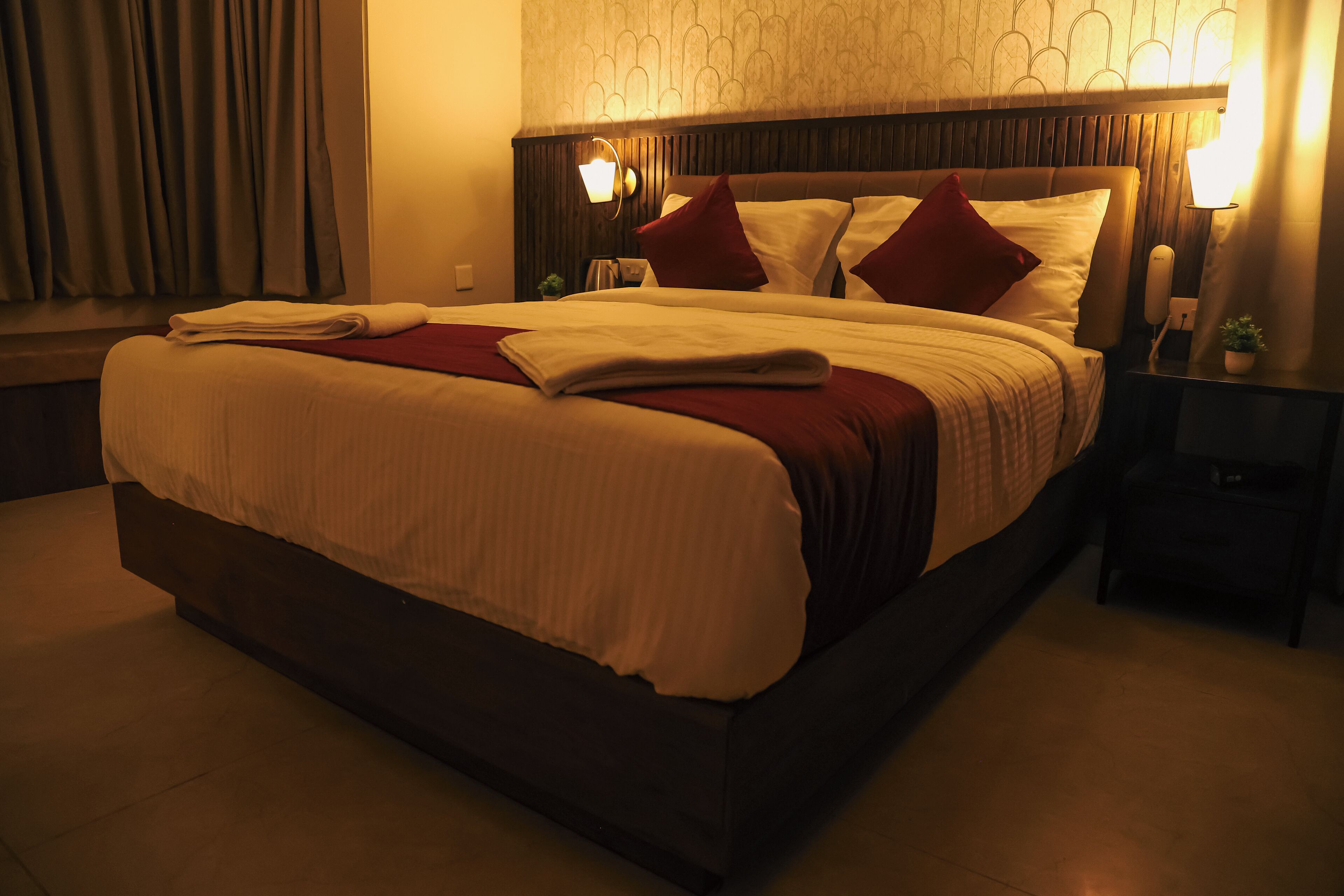 A neatly made bed with a red and white bedspread, a wooden headboard, and two bedside lamps.