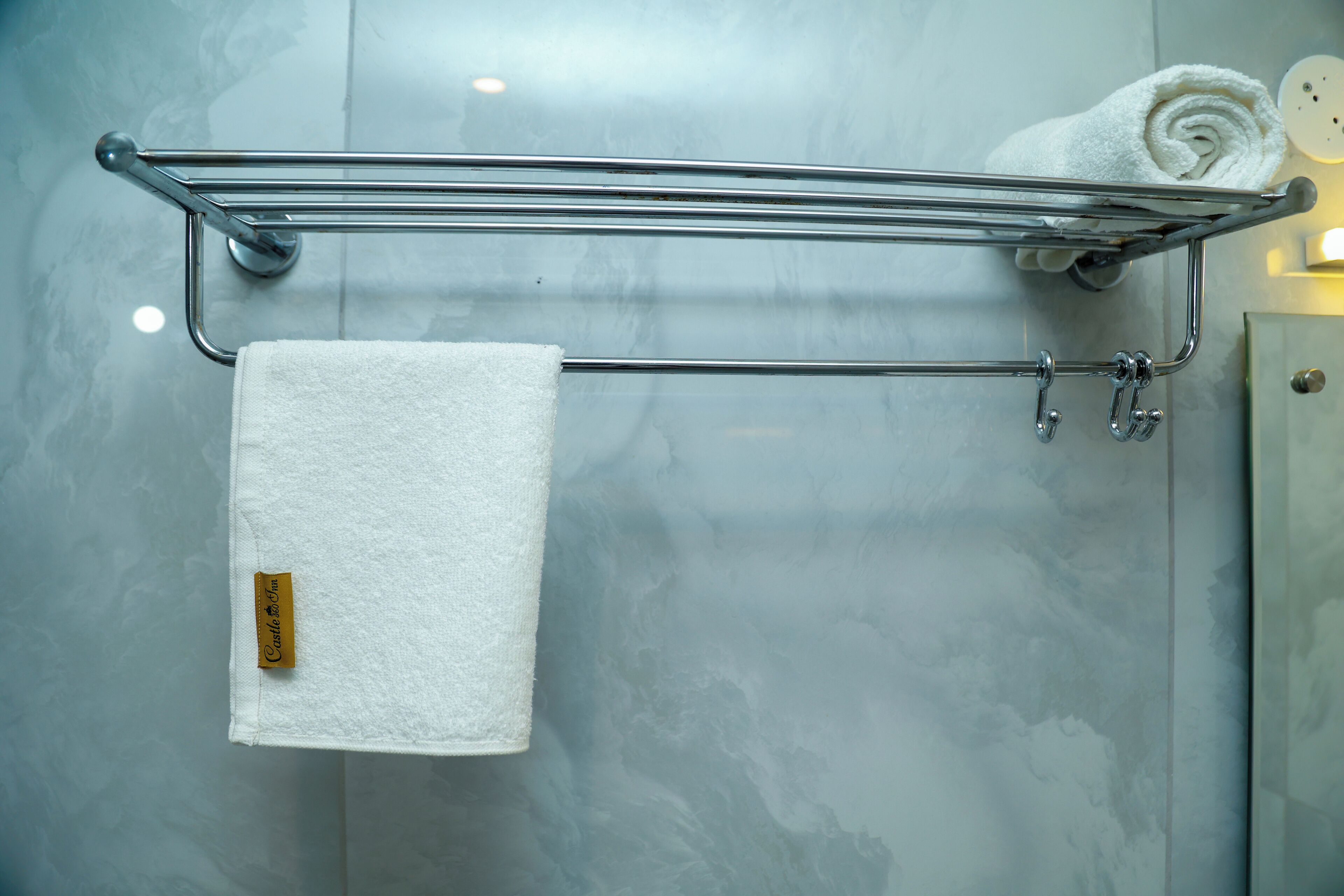 Une salle de bain avec un porte-serviettes sur lequel est posée une serviette enroulée et une serviette blanche suspendue à un crochet.
