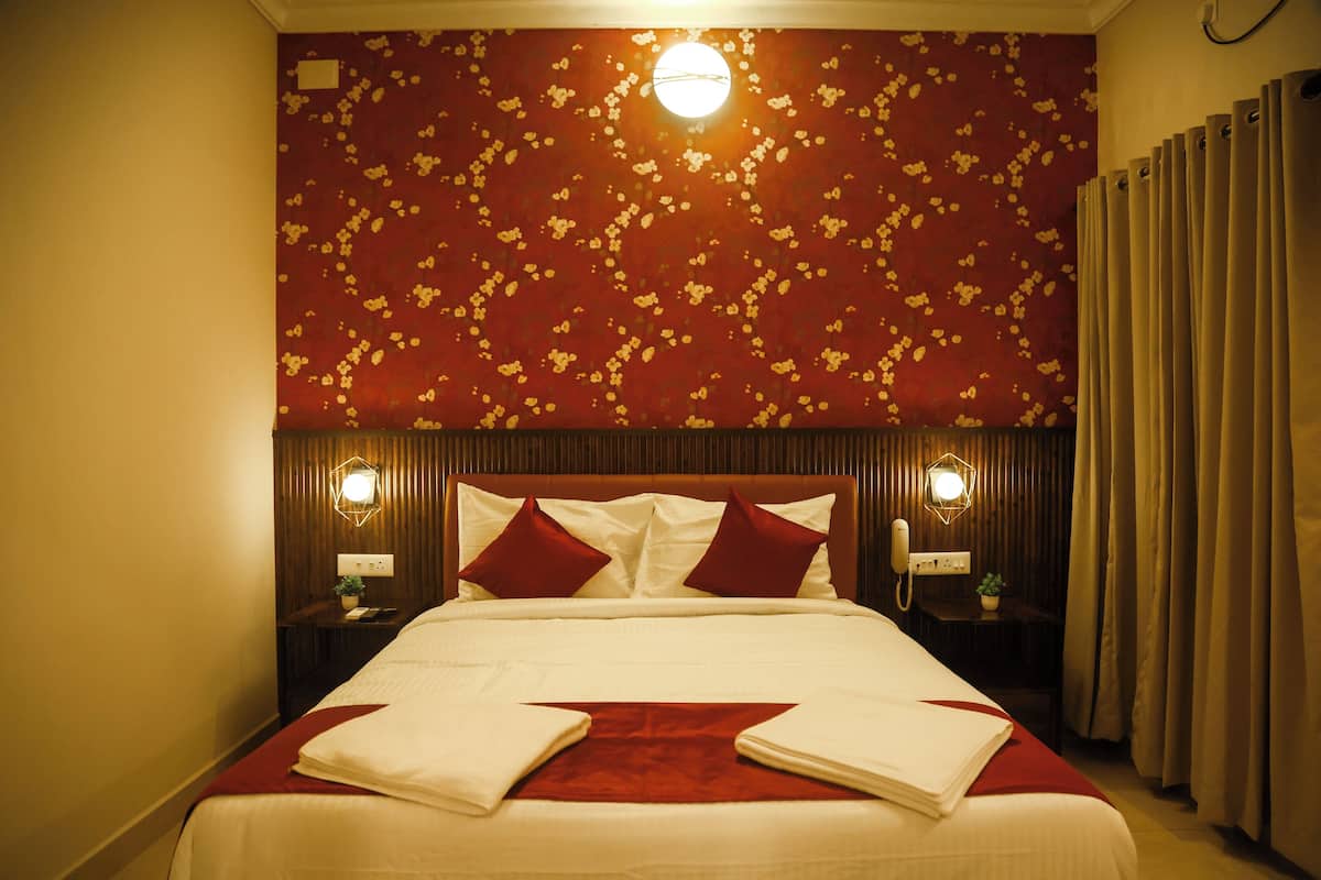 A neatly made bed with a red and white bedspread, two red pillows, and a wooden headboard. There are two bedside tables with lamps and a small plant on one.