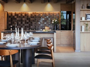 A modern kitchen with a tiled backsplash, a round dining table set with plates and glasses, and a wooden chair with a unique design.