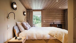 Ein Schlafzimmer mit Holzbalkendecke, einem Bett mit weißer Bettdecke, einem Nachttisch mit Kerze und einem Beistelltisch mit Kamera.