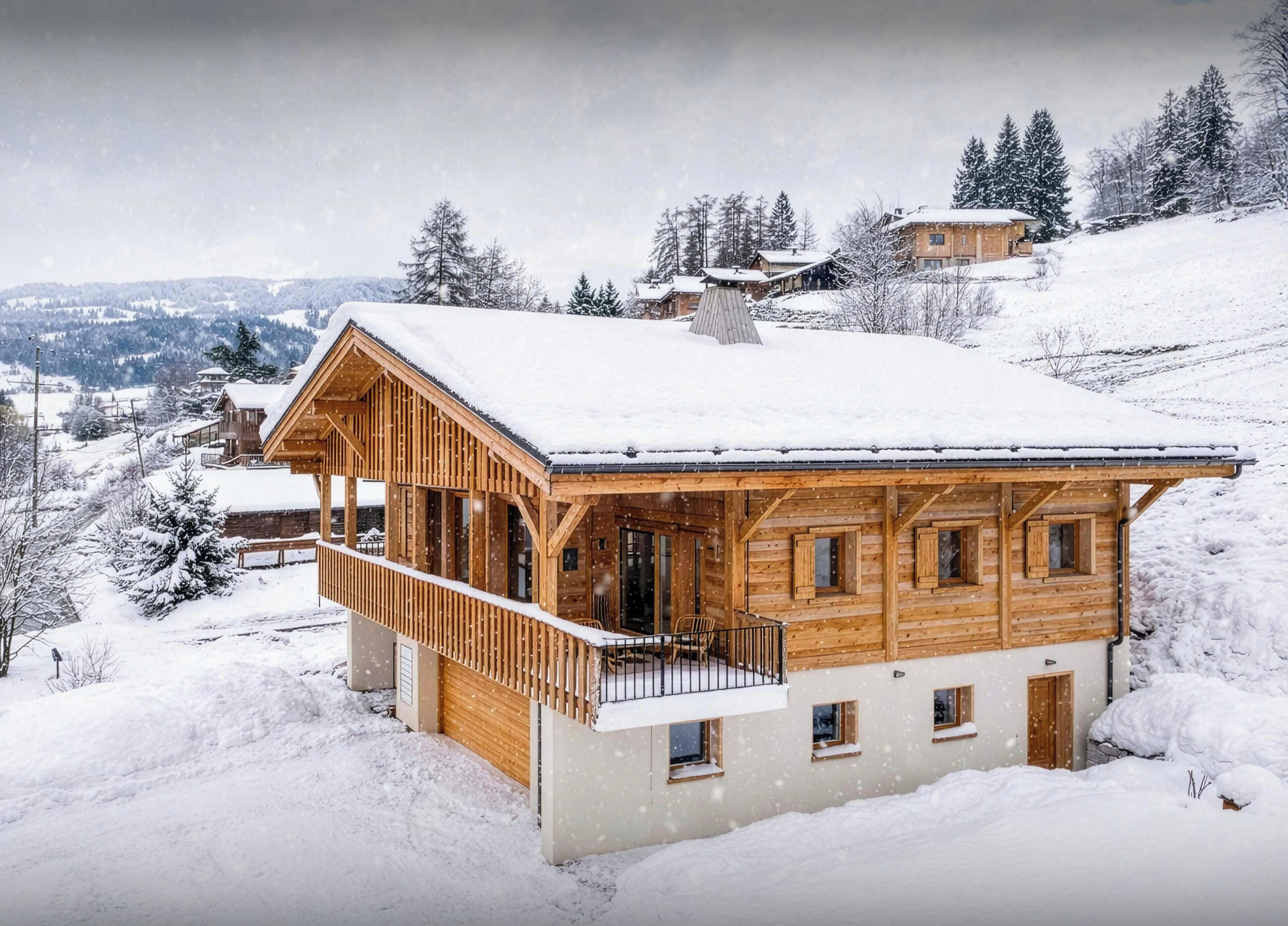 A wooden chalet with a balcony, surrounded by snow-covered trees and hills.