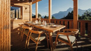 Eine Holzterrasse mit Esstisch, mit Blick auf eine Berglandschaft.