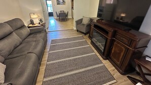 Una sala de estar con un sofá gris, un televisor, un mueble de madera y una alfombra estampada.