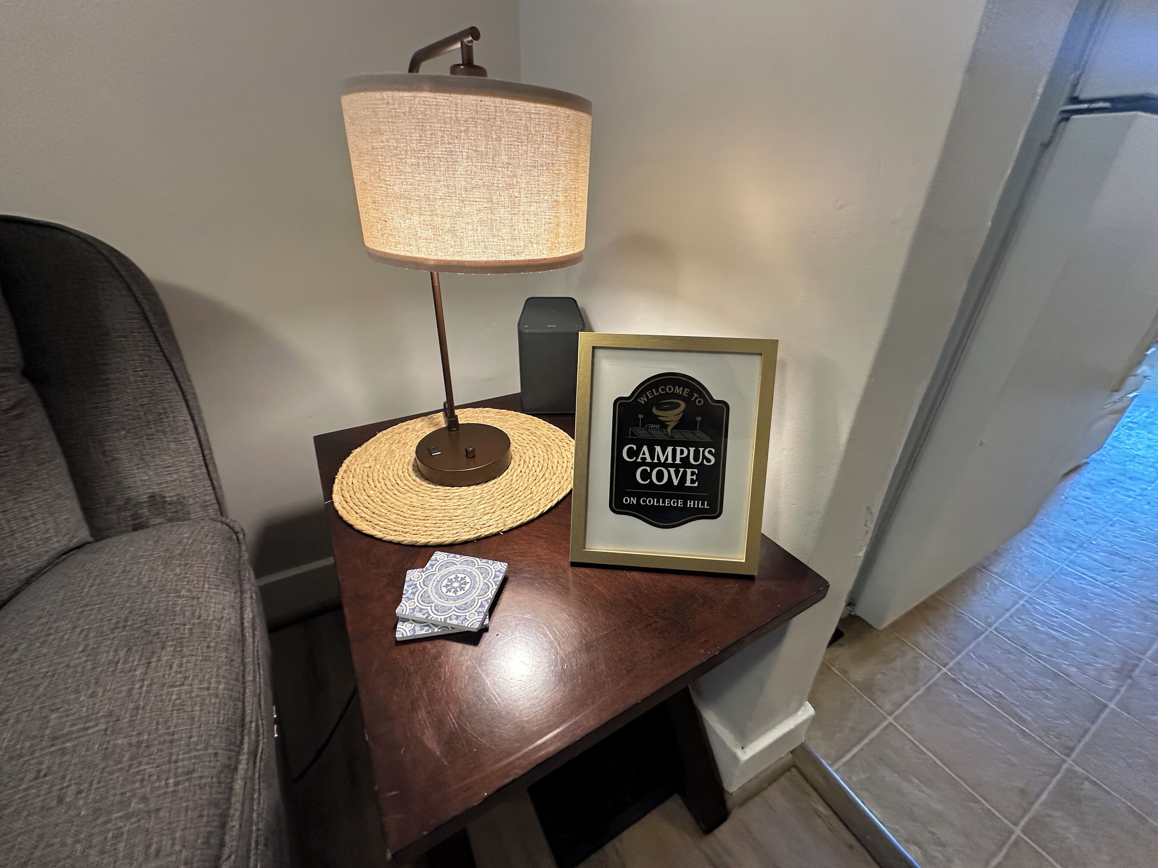 A small wooden table with a lamp, a framed welcome sign, and a decorative plate.