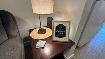 A small wooden table with a lamp, a framed welcome sign, and a decorative plate.