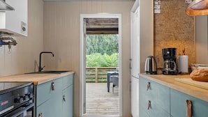 A narrow kitchen with a wooden countertop, a sink, and a Bosch stove. There is a corkboard with notes and a coffee maker on the counter.