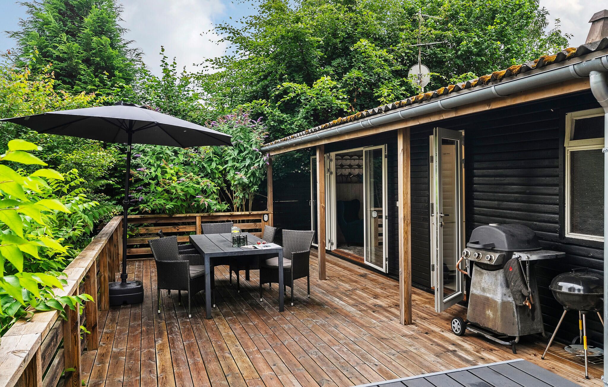 Una terraza de madera con una mesa y sillas, una parrilla y un área cubierta con una sombrilla.