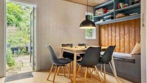 A dining area with a wooden table and chairs, a pendant light, and a bookshelf with various items.