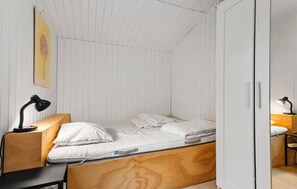 A small, single-bed room with a wooden headboard, a desk with a lamp, and a wardrobe.