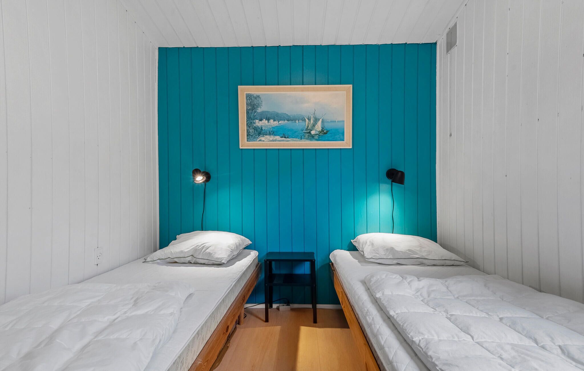 Une petite chambre agréable, dotée de deux lits simples, d’un bureau et d’un tableau au mur.