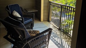 A balcony with wicker chairs and a small table, overlooking a lush green area.
