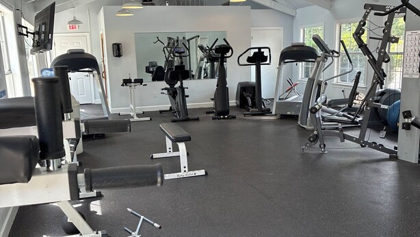 A gym with various exercise equipment, a large mirror, and a door with an exit sign.
