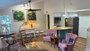A living room with a sofa, chairs, a coffee table, and a dining area with a table and chairs. There is a kitchen area with cabinets and appliances.