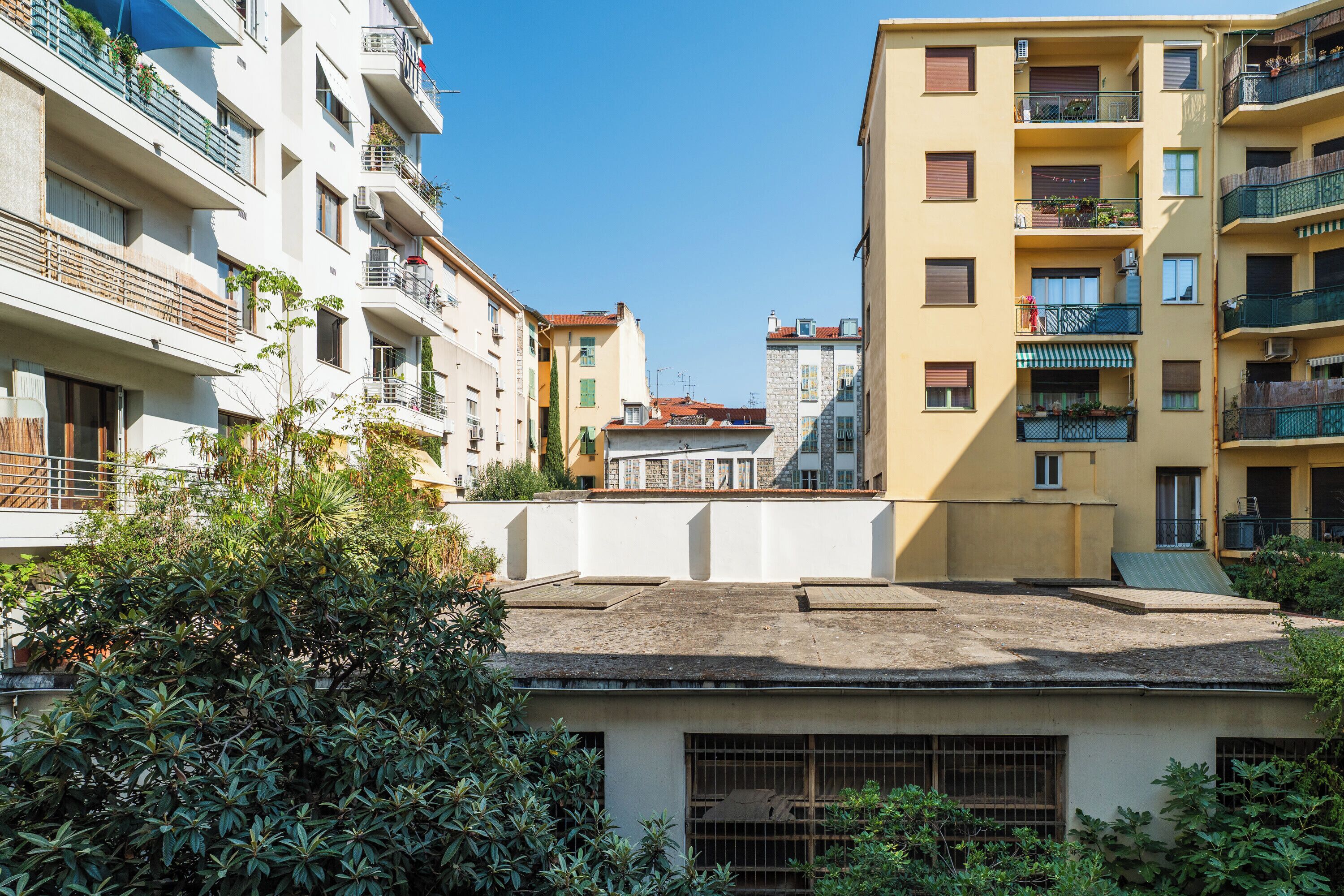 Um edifício residencial de vários andares com varandas, um telhado plano e uma pequena área de jardim.
