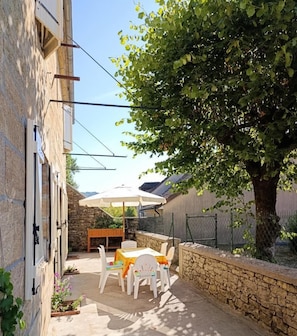 A courtyard with a stone wall, a tree, and a table with chairs.