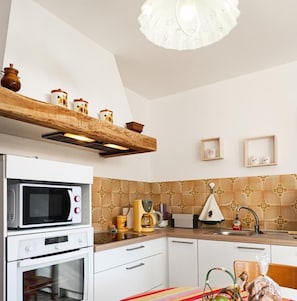 A kitchen with a microwave, oven, and coffee maker on the countertop, a striped tablecloth, and a hanging light fixture.