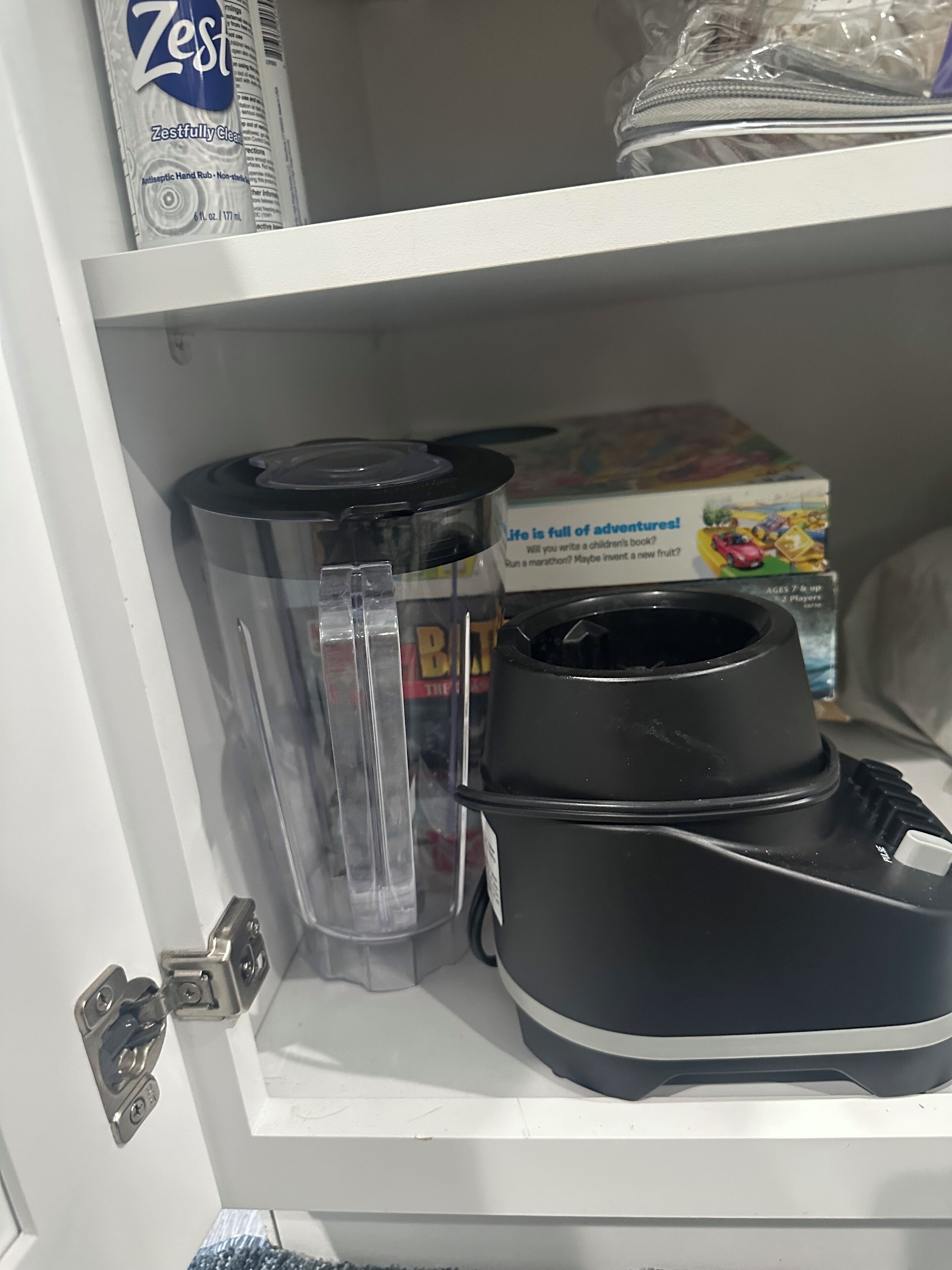 A kitchen cabinet with a blender, a box of Zest hand soap, and a children's board game.