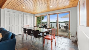A dining area with a wooden ceiling, a large table with chairs, and a view through glass doors to an outdoor patio. - White Lake MI Lakeside Home, Hot Tub, Pet Friendly (White Lake Township)