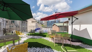 An outdoor patio area with green and red umbrellas, outdoor seating, and a view of buildings in the background. - Hi Seodaemun (Seoul)