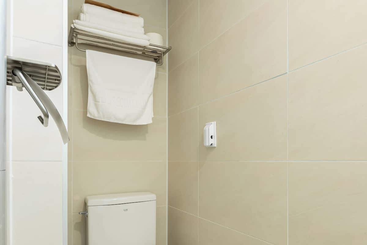 Un baño pequeño y limpio con inodoro, un estante con toallas y un cubo de basura.