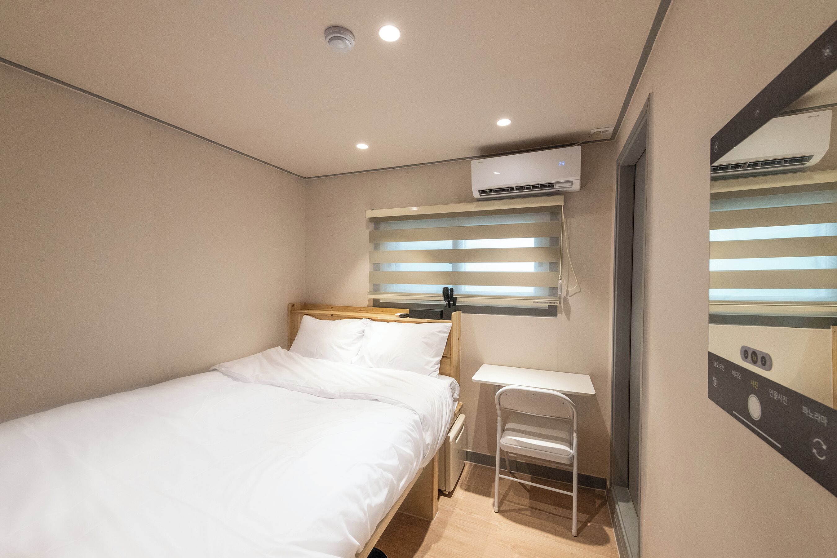 A compact hotel room with a single bed, a small desk, and a wall-mounted air conditioner.