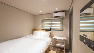 A compact hotel room with a single bed, a small desk, and a wall-mounted air conditioner.
