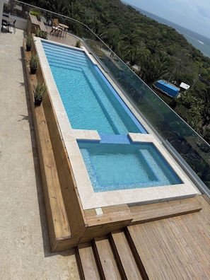 A rectangular pool with a wooden deck and potted plants, surrounded by lush greenery and overlooking a coastal landscape. - Penthouse at Duna Tower with Incredible Views (Crawfish Rock)