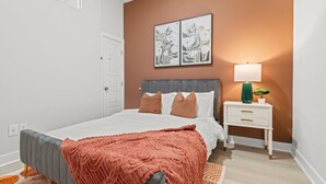 Ein Schlafzimmer mit einem Bett, einem Nachttisch, einer Lampe und einer Wand mit zwei gerahmten Kunstwerken.
