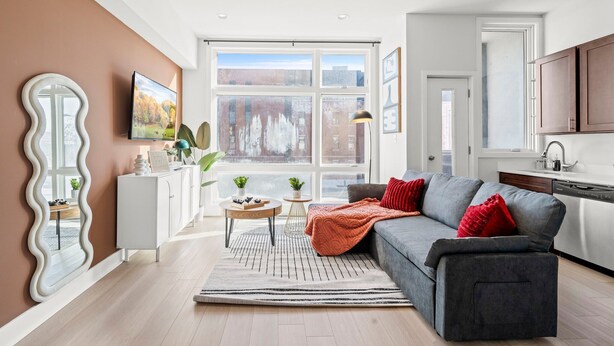 Ein modernes Wohnzimmer mit einem grauen Sofa, roten Kissen, einem großen Spiegel und einem Fernseher.