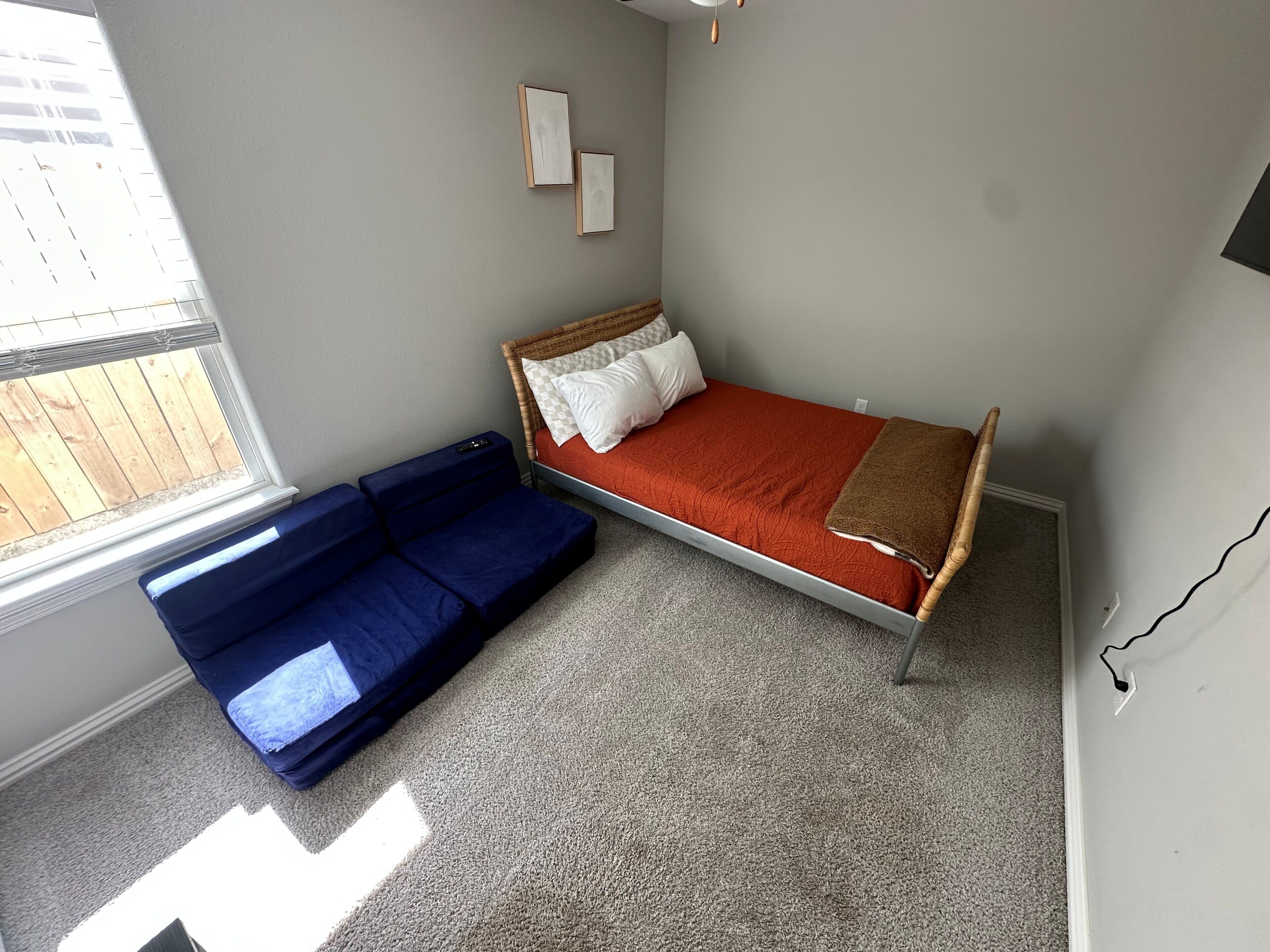 A bedroom with a bed, a blue sofa, a window, and a wall-mounted picture.