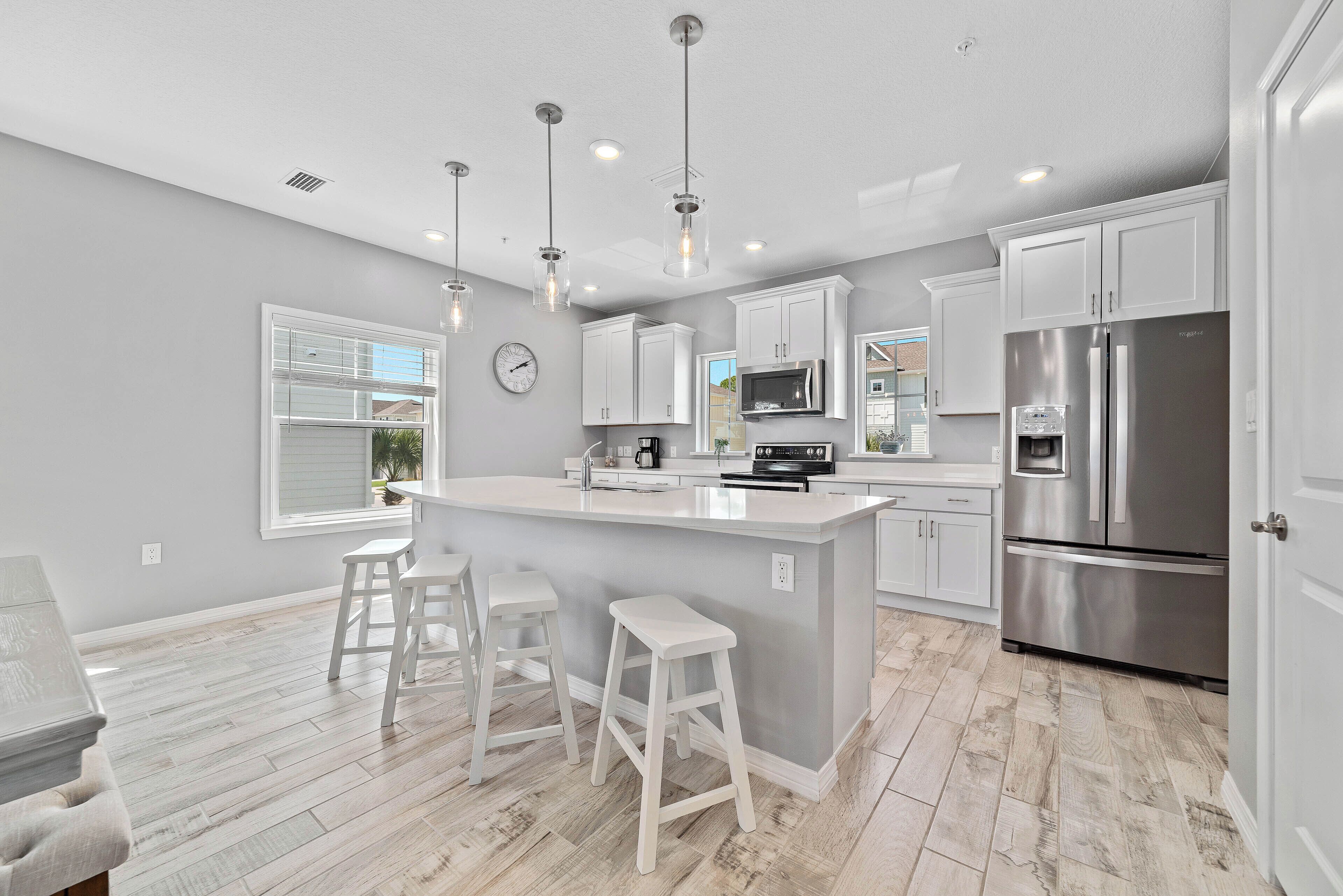 Una cocina moderna con armarios blancos, electrodomésticos de acero inoxidable y una isla central con taburetes.