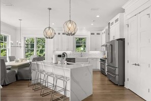 A modern kitchen with white cabinetry, a central island with bar stools, stainless steel appliances, and pendant lighting.