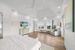 Une chambre spacieuse avec un grand lit, un coin salon avec un banc et une vue sur l’extérieur grâce à de grandes fenêtres.