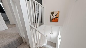 A staircase with white railings leading to a landing with a door and a wall-mounted abstract painting.