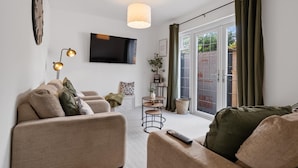 A modern living room with a sofa set, a flat-screen TV, a pendant light, and a sliding glass door leading to an outdoor area.