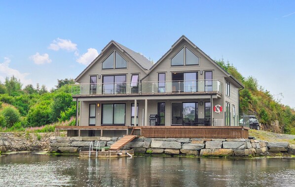 A two-story house with a balcony, large windows, and a stone foundation near a body of water. - 5 bedroom gorgeous home in Bremnes (Bremnes)